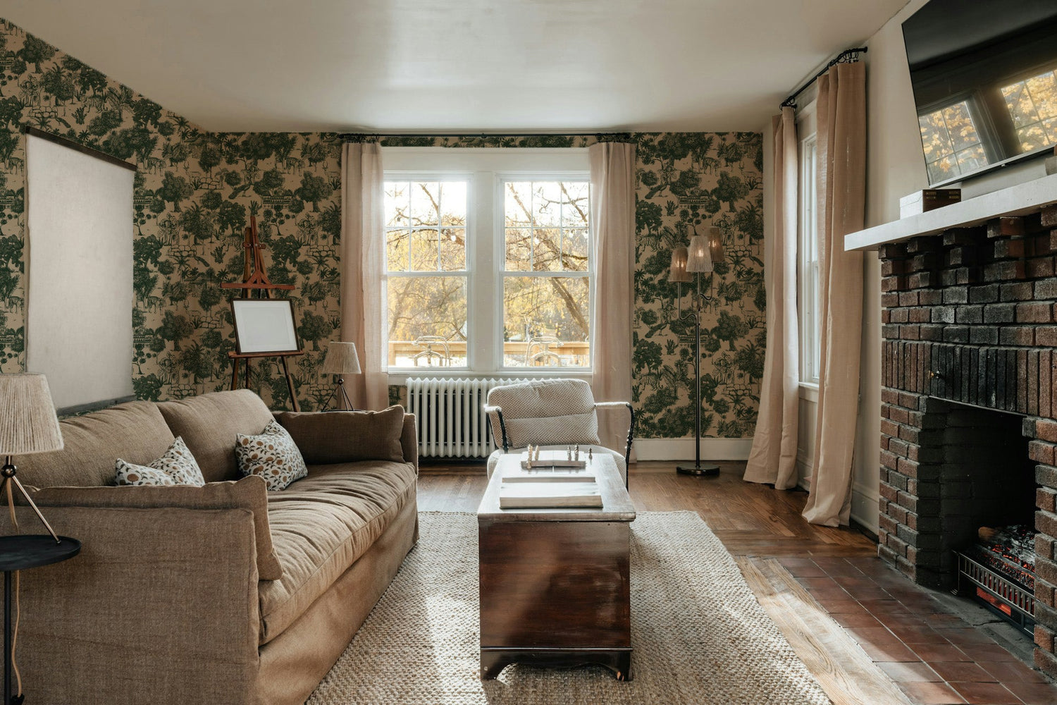 Living room with Jungle Toile Green wallpaper, brown sofa, and brick fireplace.