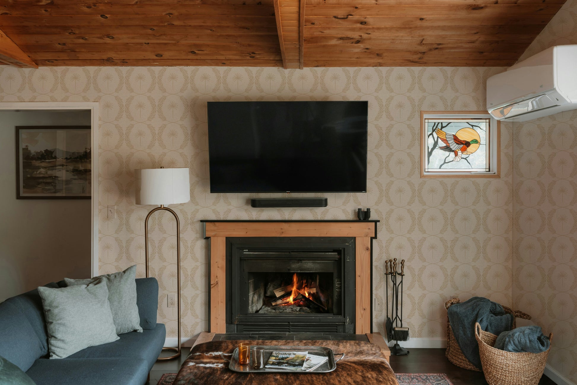 Living room with Palm Wreath Cream wallpaper, fireplace, and TV.