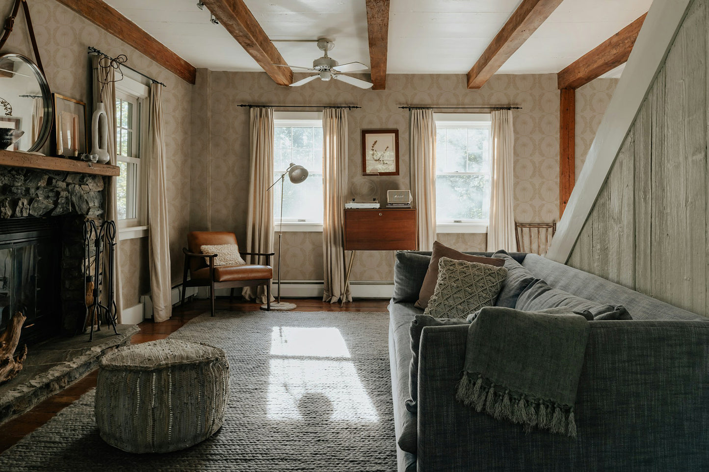 Living room with Palm Wreath Cream wallpaper, wood beams, and cozy furnishings.