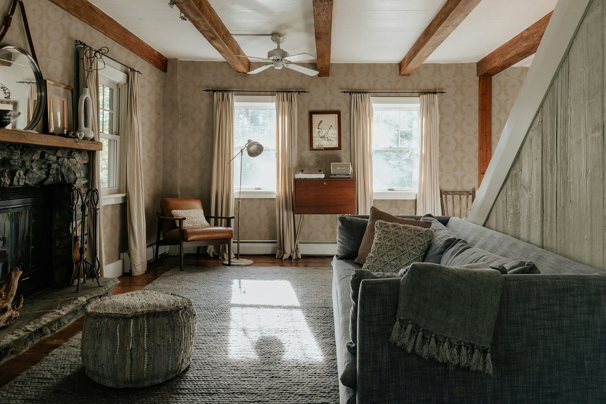 Living room with Palm Wreath Cream wallpaper, wood beams, and cozy furnishings.