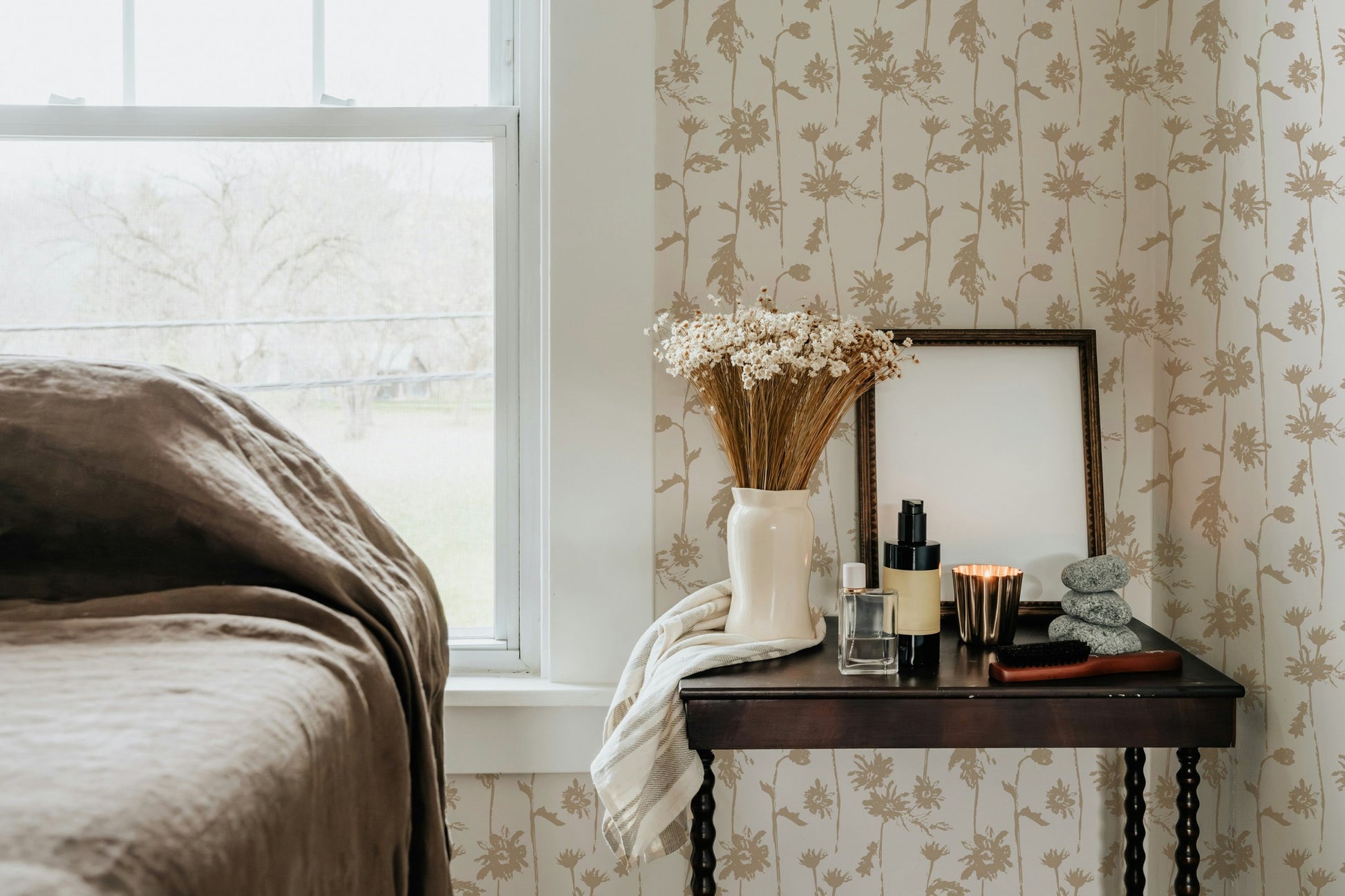 Beige floral wallpaper in cozy bedroom with vase and table decor.