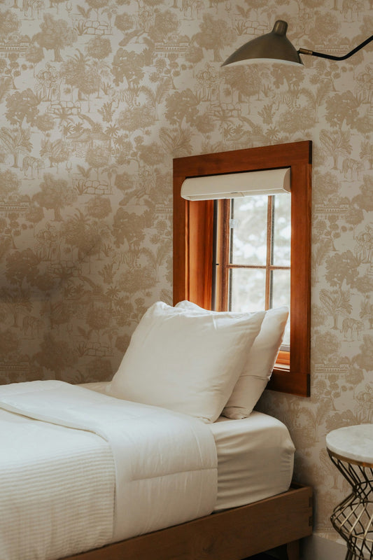 Cream jungle toile wallpaper with tigers and trees in cozy bedroom setting.
