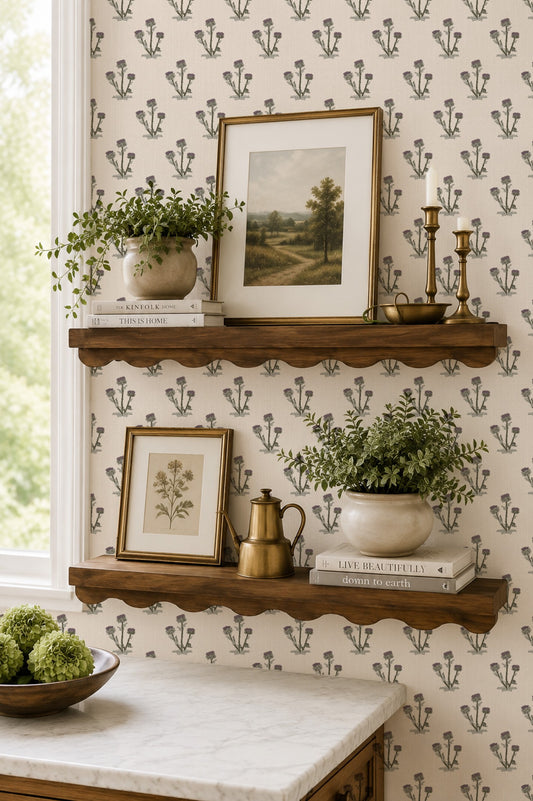 Cream wallpaper with thistle pattern, wooden shelves, plants, and framed art in a cozy room.