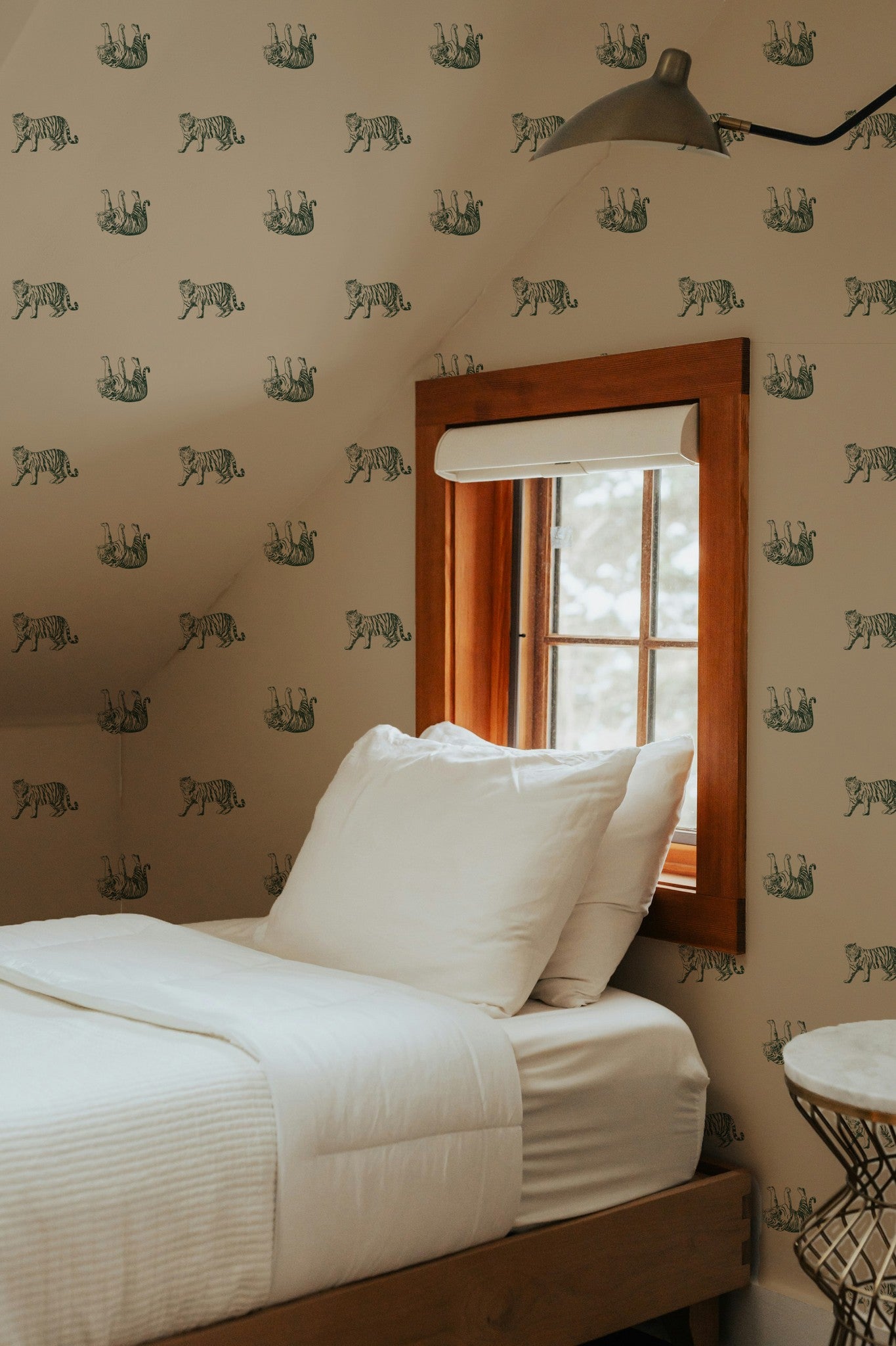Bedroom with green tiger pattern wallpaper on muted gold, wooden bed frame, and window.
