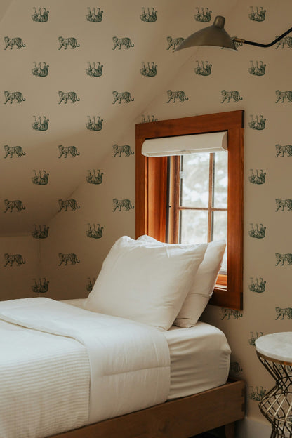 Bedroom with green tiger pattern wallpaper on muted gold, wooden bed frame, and window.