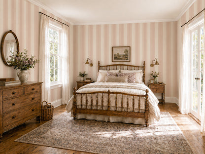 Vintage bedroom with pink and cream striped wallpaper, lace detailing, and wooden furniture.