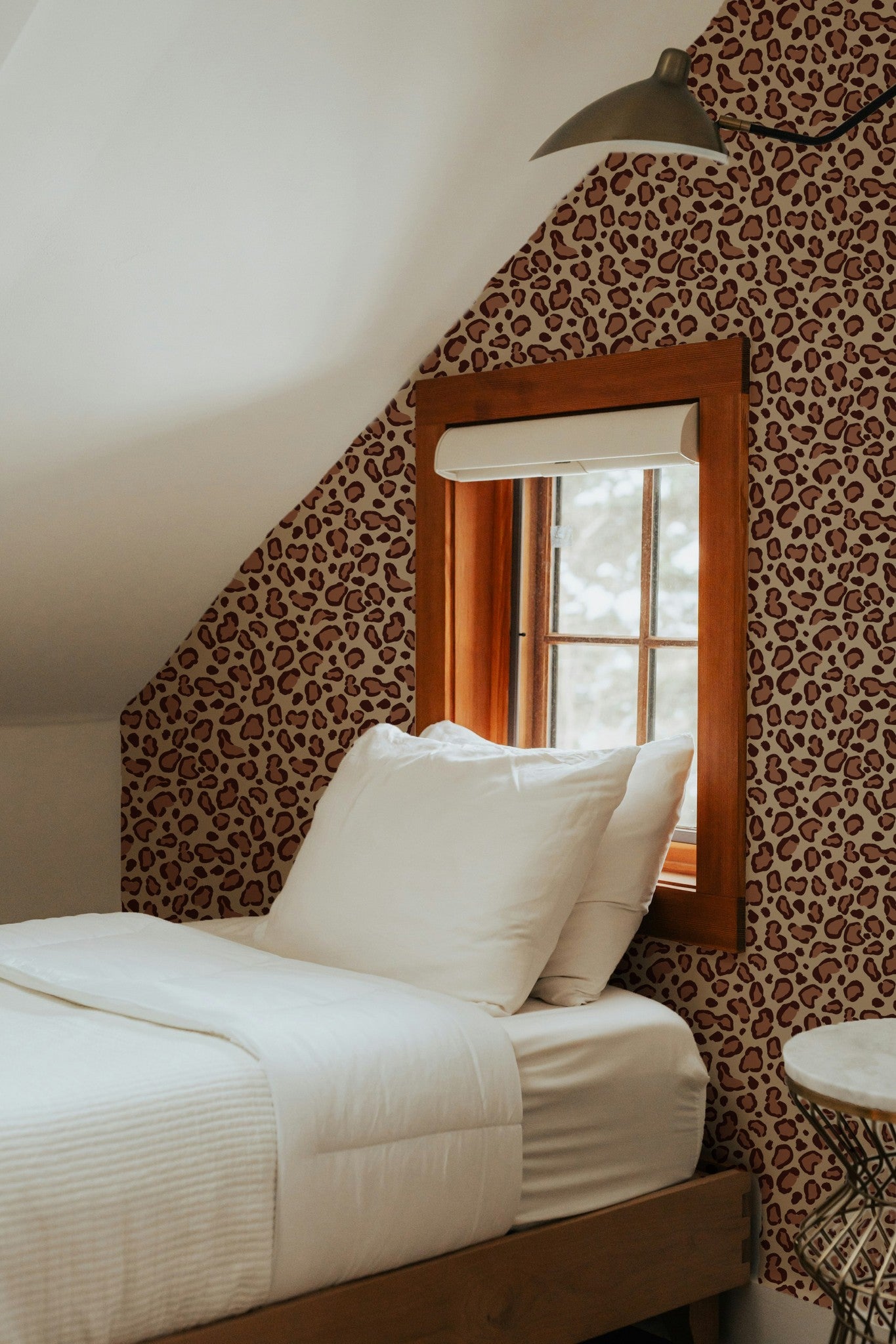 Leopard print brown wallpaper in cozy bedroom with white bedding and wooden window frame.