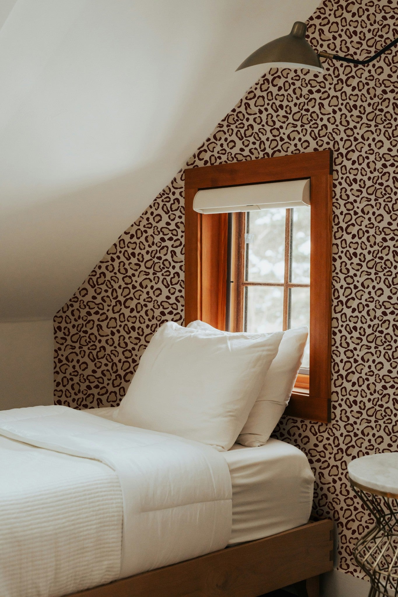 Leopard print cream wallpaper in cozy attic bedroom with wooden window frame.