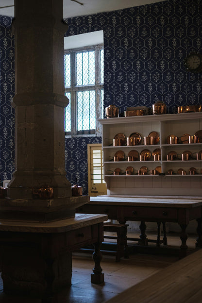Navy floral trellis wallpaper in vintage kitchen with wooden tables and copper pots.