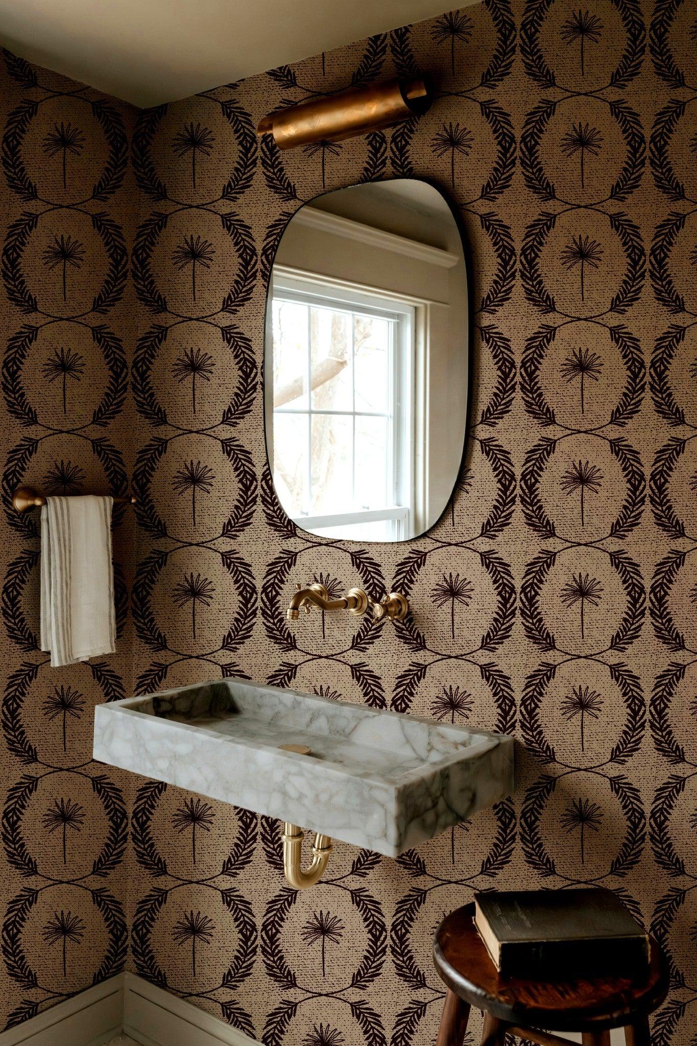 Palm wreath red wallpaper in bathroom with marble sink and oval mirror.