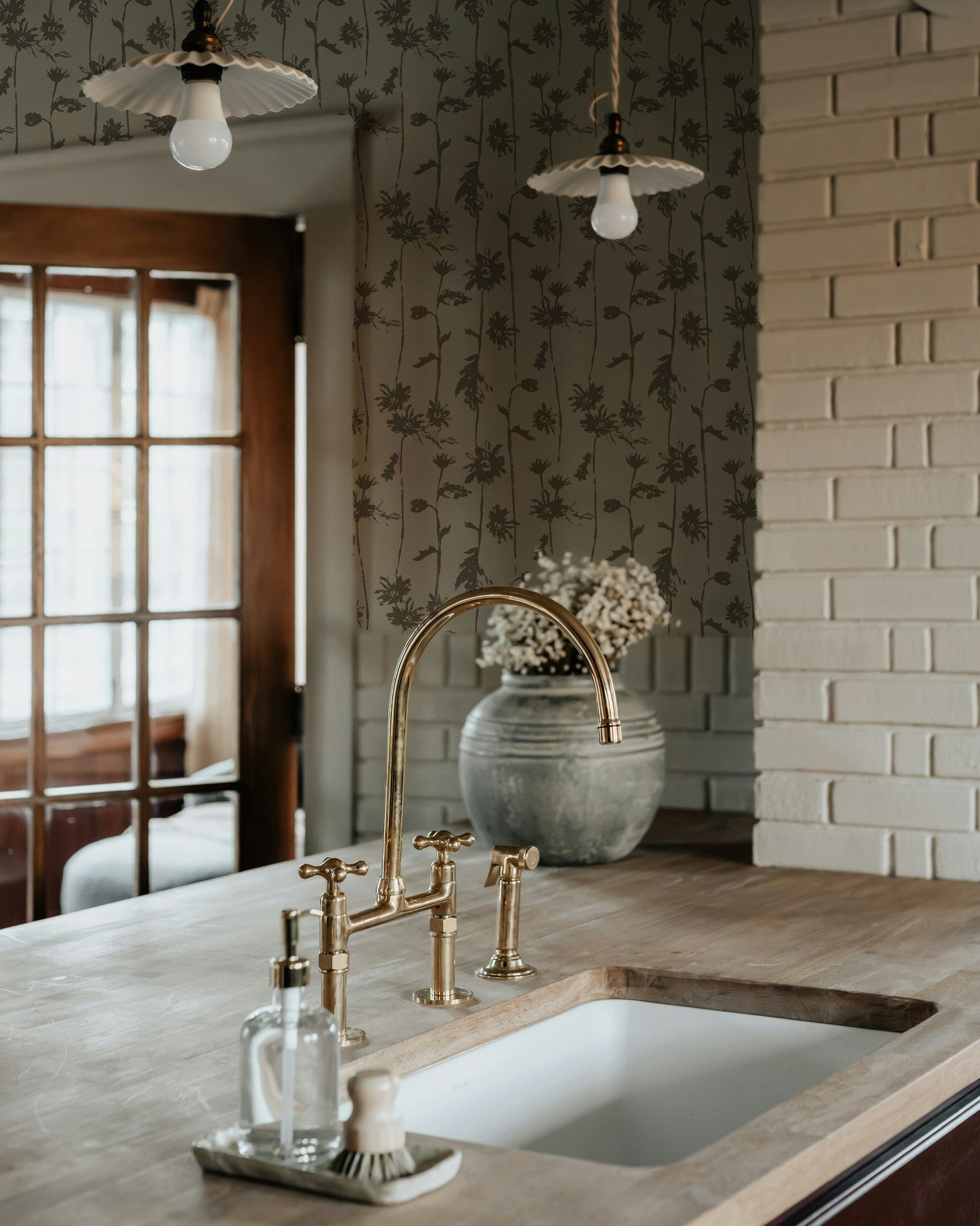 Sage green floral wallpaper in rustic kitchen setting with brass fixtures.
